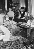 Två barn och en man öppnar sina julklappar vid granen. Okända personer, plats och årtal.