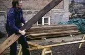 En man lyfter en bräda. Exteriörfoto från upprustningen av Mölndals Museum på Norra Forsåkersgatan 19 (Kallkällan 1) år 1985.