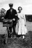 Frans Algot Holm, indelt soldat och kyrkväktare i Vrigstad, började
den 1 december 1912 som lantbrevbärare på linjen Vrigstad - Horveryd
- Hjärtetorp - Gettersryd - Bjällebo - Virestorp - Porsamålen -
Trismålen - Åkaköp - Vrigstad. Turen gick han två gånger i veckan,
till en början till fots, men så småningom per cykel. På vintrarna
måste han köra med häst. Han slutade som lantbrevbärare den 31 juli
1939 och efterträddes av sin son Albin. Bilden är tagen 1933 vid
Borstabygget som han passerade utefter linjen. Här bodde gode vännen
före detta grenadjären Oscar Ceder. Det är Ceders dotter Alice, som
krokar arm med lantbrevbärren.