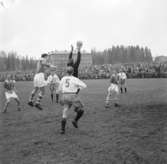 En målvakt hoppar upp för att fånga bollen i en fotbollsmatch.