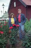 Karin Nilsson och hennes man står bland buskar och rosor utanför ett hus i Stockmakarbyn i Huskvarna.