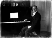 Rumsinteriör, en man vid pianot.
Pastor Petrus Sangéus