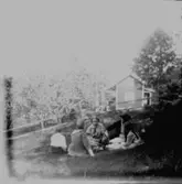 Fika i gröngräset, sex personer.
Sommarstugan Fridensborg i bakgrunden.