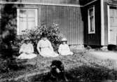 Bostadshus, en kvinna och två barn framför huset, en hund.