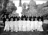 17 konfirmander, 9 flickor,   8 pojkar och kyrkoherde Johansson.
Glanshammars kyrka och klockstapel i bakgrunden.
