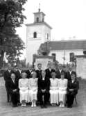 13 konfirmander, 4 flickor, 9 pojkar varav en i uniform och pastor Hilding Hasselmyr.
Tysslinge kyrka i bakgrunden.