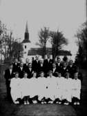 20 konfirmander, 8 flickor, 12 pojkar och kyrkoherde Sköldebrand.
Kils kyrka i bakgrunden.
Pingstdagen den 13 maj 1951.