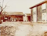 Knuttimrade ekonomibyggnader, radby. 
Tre personer framför timmerbyggnaden.
Helins gård. 
Kopia 1950 till Nordiska Museet.