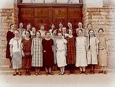 Norra Folkskolan, Högre Folkskolan eller Fortsättningsskolan, 20 skolflickor med lärare, sal 36, klass 3A. Skolbyggnad i bakgrunden.
Eva Ingvaldsson