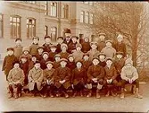 Västra skolan, 32 skolpojkar med lärare, sal 2.
Skolbyggnad i bakgrunden.
J. Norelius
