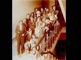 Rumsinteriör, 19 utklädda damer i trappan.
Doktor Winberg