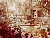Sommarstuga vid en bäck.
En kvinna och två flickor på bron.
Disponent Carl Källen