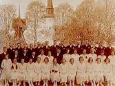 Konfirmander, 21 flickor, 18 pojkar och prästen.
Glanshammars kyrka i bakgrunden.