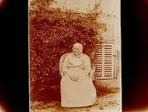 Äldre kvinna.
Bostadshus i bakgrunden.
Nordfeldt