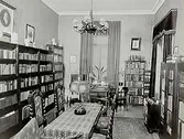 Biblioteksinteriör.
Fru Apotekare Dahl.