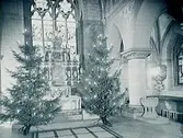 Interiör av Nikolaikyrkan, dekorerad med två julgranar framme i koret.
Taget för Röda Korset till vykort.