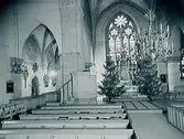 Interiör av Nikolaikyrkan, dekorerad med två julgranar framme i koret.
Taget för Röda Korset till vykort.