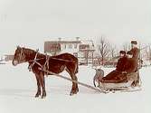 Häst spänd för släde, 3 personer i en släde.Bostadshus i bakgrunden.Gustaf Wennerlund