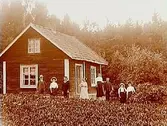 Enkelstuga, 8 personer framför stugan.
Karl Persson