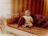 Ett litet barn med en hund i soffan.Elof Dahm