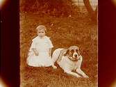 En liten flicka med en stor hund i gräset.A.G. Södervall