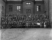 Nya Skofabriks AB Örnen, bolagets verkställande direktör, tjänstemän, förmän och arbetspersonal.
Fabriksbyggnaden i bakgrunden.