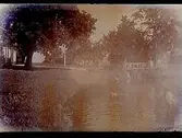 Tvåvånings bostadshus, bron över ån, dammen med fåglar i, en man med hund på bron.
E. Vedfelt