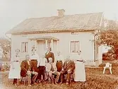 En och en halvvånings bostadshus med förstubro i snickarglädje.
9 personer framför byggnaden.
Gustaf Johansson