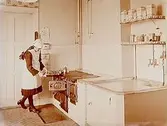 Duberg & Söner Värme & Sanitetsfirma.
Köksinteriör med en kvinna som demonstrerar järnspisen Ello. Patent Örebro Nr.6.