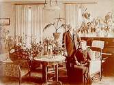 Rumsinteriör, en man och en kvinna bland blommor.
Direktör Erik Edman