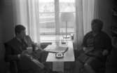 Frisörgrej, Bandy, Yvonne Hinseberg 15 november 1967

I ett rum sitter en man i kostym och har ett skrivblock i handen. Mittemot honom sitter en kvinna i klänning på Hinsebergs kvinnofängele.