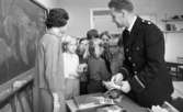 Första spad, Polis i skolorna 13 okt 1967

Polisman håller informationsmaterial i handen som skall delas ut till eleverna. Läraren står vid svarta tavlan.