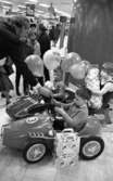 Krämaren 5 år 26 mars 1968

Två pojkar sitter i trampbilar och har fått ballonger och spargris av en man i kavaj. En flicka sitter på en gunghäst med ett paket och ballong. I bakgrunden ser man kunder.