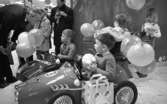 Krämaren 5 år 26 mars 1968

En man står vid en pelare med en kamera. Två pojkar sitter i trampbilar med ballonger och spargris. En flicka har en dockvagn och en annan flicka sitter på en gunghäst.