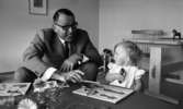 Barndaghem 9 september 1966

Vid ett bord sitter en flicka och en man i grå kostym och lägger pussel. På bordet står det blommor i en vas.