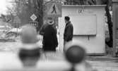 Gyttorp 2 23 februari 1967

Vid ett övergångsställ står en kvinna och två män.
Bakom dem ser man en telefonkiosk, och ett biltak med
lampor.