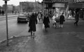 Gående, första felgångarn 7 februari 1967 

Vid Järntorget ser man biltrafik gångende. En kvinna med barnvagn. Skyltfönster från två affärer. I bakgrunden syns Stora Hotellet.