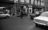 Gående, första felgångarn 7 februari 1967

På Drottninggatan står det bilar parkerade, och en bil kommer körande. Det går också en man över gatan.