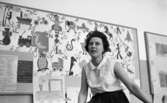 Kopparbergs skola, 1 mars 1967. En lärarinna som sitter i ett klassrum. Hon är klädd i en vit blus och en svart veckad kjol. I bakgrunden hänger en anslagstavla med varje bokstav i alfabetet, barnteckningar m.m.

Fröken Karin Flodström