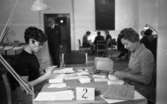 Rösträkning.24 september 1968

Kvinnor utför rösträkning vid ett av av flera bord i samlingssal.