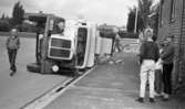 Sopbil välte 27 juli 1965

En sopbil har vält och ligger på sidan på en gata nära trottoaren. En folksamling har uppstått invid den.