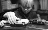 Minibilar, 7 december 1965

I förgrunden syns leksaksracerbilar som en pojke leker med. Han kör bilarna på en leksaksbilbana.