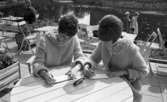 Systrarna Rynning igen, 7 juli 1965

På ett kafé vid Svartån nära Örebro slott sitter två kvinnor vid ett bord och skriver vykort. De är klädda i stickade koftor.
