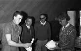 Drick vin gratis 31 juli 1965

En kvinna i klänning och glasögon samt tre män står i en lokal. Kvinnan håller i en stor porslinsterrin och en av männen håller i en porslinsljusstake. De två andra männen tittar på porslinsljusstaken.