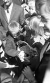Knytkalaset 5 juli 1965.

En jubileumsvärdinna i förgrunden. Ett barn i bakgrunden håller i en korg med en kattunge i. Ett annat barn klappar kattungen. Flera barn och vuxna står runtomkring.