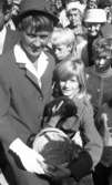 Knytkalaset 5 juli 1965.

En jubileumsvärdinna och en liten flicka håller gemensamt i en korg. Den lilla flickan har också en kattunge i famnen. Andra barn och vuxna står runtomkring dem.