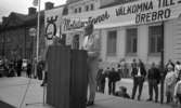 Knytkalaset 5 juli 1965.

Herre håller tal på scenen. Harald Aronsson står bredvid. 
I fonden Norlings bryggeri, Näbbtorgsgatan 12.