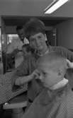 Damfrisörskor 8 juli 1965.

I förgrunden klipper en damfrisörska håret på en liten pojke. I bakgrunden klipper en manlig frisör håret på en ung herre.