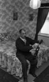 Hemma hos Karasko, 24 december 1965

Familjefar Karasko sitter på en dubbelsäng och stämmer en fiol. Han är rom. I bakgrunden hänger två tavlor på väggen. Ett fönster med gardiner syns även genom vilket man skymtar ett snöigt landskap. På sängen ligger ett sängöverkast samt två kuddar. På golvet finns två mattor.