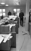 Handelsbanken Fellingsbro, 11 december 1965 

Fyra kostymklädda unga män inne på Handelsbanken i Fellingsbro. Träbitar, verktyg och papper ligger kringströdda på disken och skåpen. Lokalen och inredningen är under uppbyggnad.